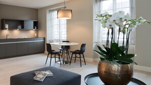Een moderne keuken met donkere kastjes, een eethoek met een ronde tafel en stoelen, en een groot raam met gordijnen.