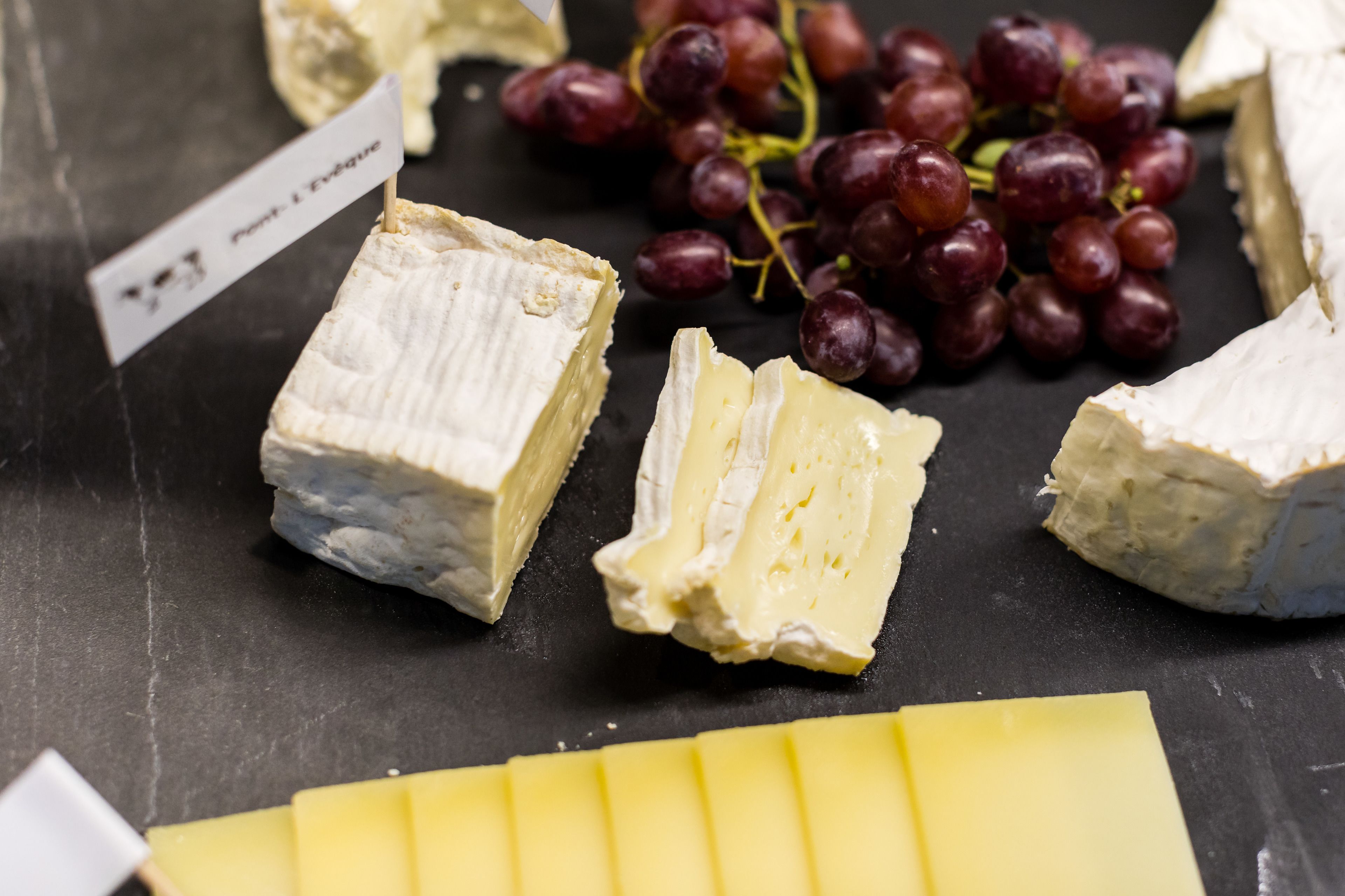 Diversos tipos de queso y uvas sobre una superficie negra.