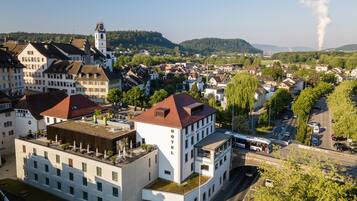 Ein Hotel mit Dachterrasse, einem im Hintergrund sichtbaren Glockenturm und Blick auf eine Stadt mit Fluss und Bergen.