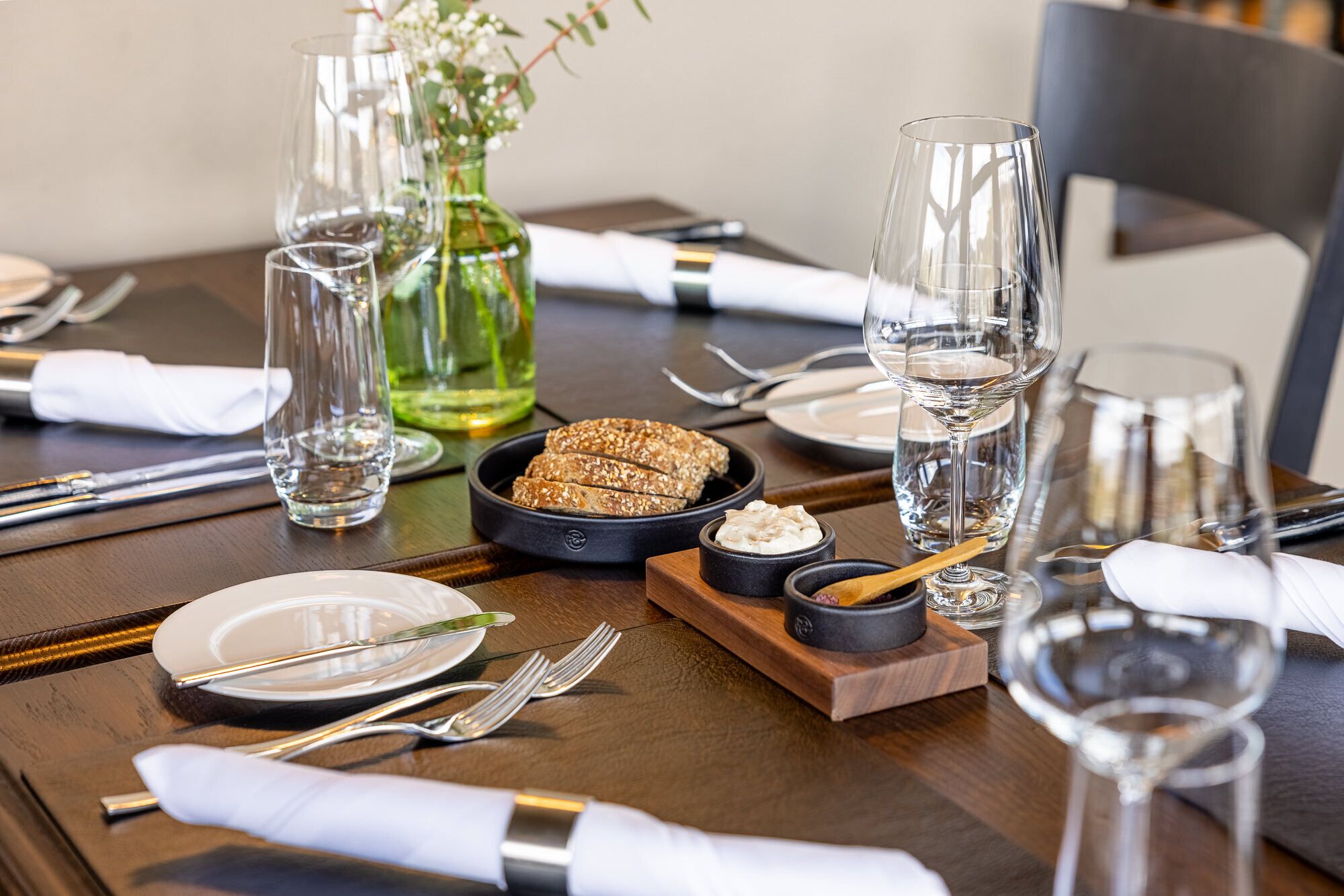 Una mesa puesta con platos, cubiertos, vasos y un bol de pan.
