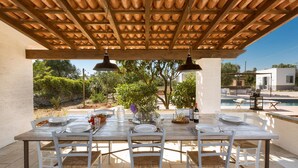 Ein Essbereich im Freien mit einer Holzpergola, weißen Stühlen und einem Tisch für vier Personen.