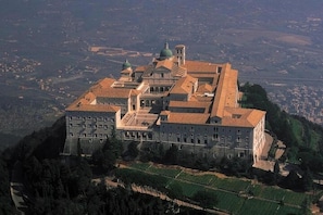 A large, historic building with multiple domes and a prominent central tower, surrounded by lush greenery and a hilly landscape. - Hotel Ristorante La Campagnola (Cassino)
