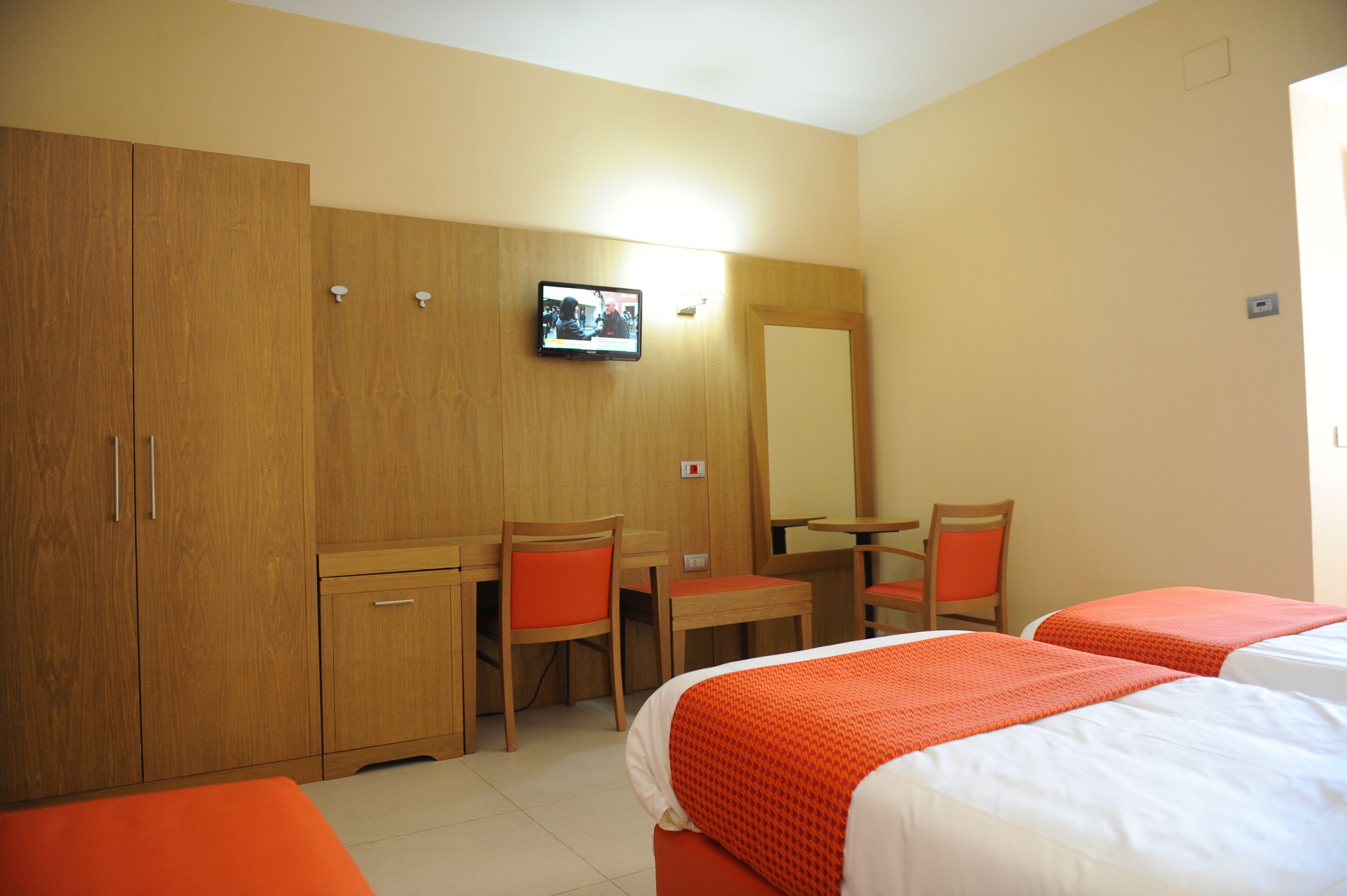Ein Hotelzimmer mit Holzmöbeln, einem Fernseher und zwei Betten mit orangefarbener Bettwäsche.