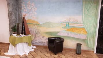 Una habitación con un mural de un paisaje, una mesa con una planta y una botella, una silla y una cortina.