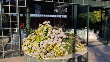 Un edificio con grandes ventanales y un parterre circular lleno de flores rosadas.