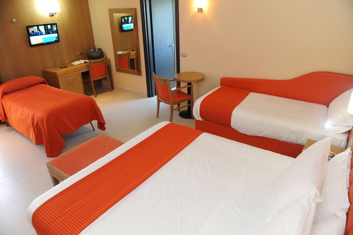 Ett hotellrum med två separata sängar, ett skrivbord, en stol, en TV och en dörr.
