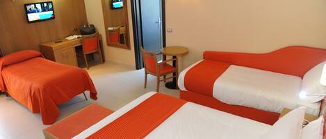 A hotel room with two single beds, a desk, a chair, a TV, and a door.
