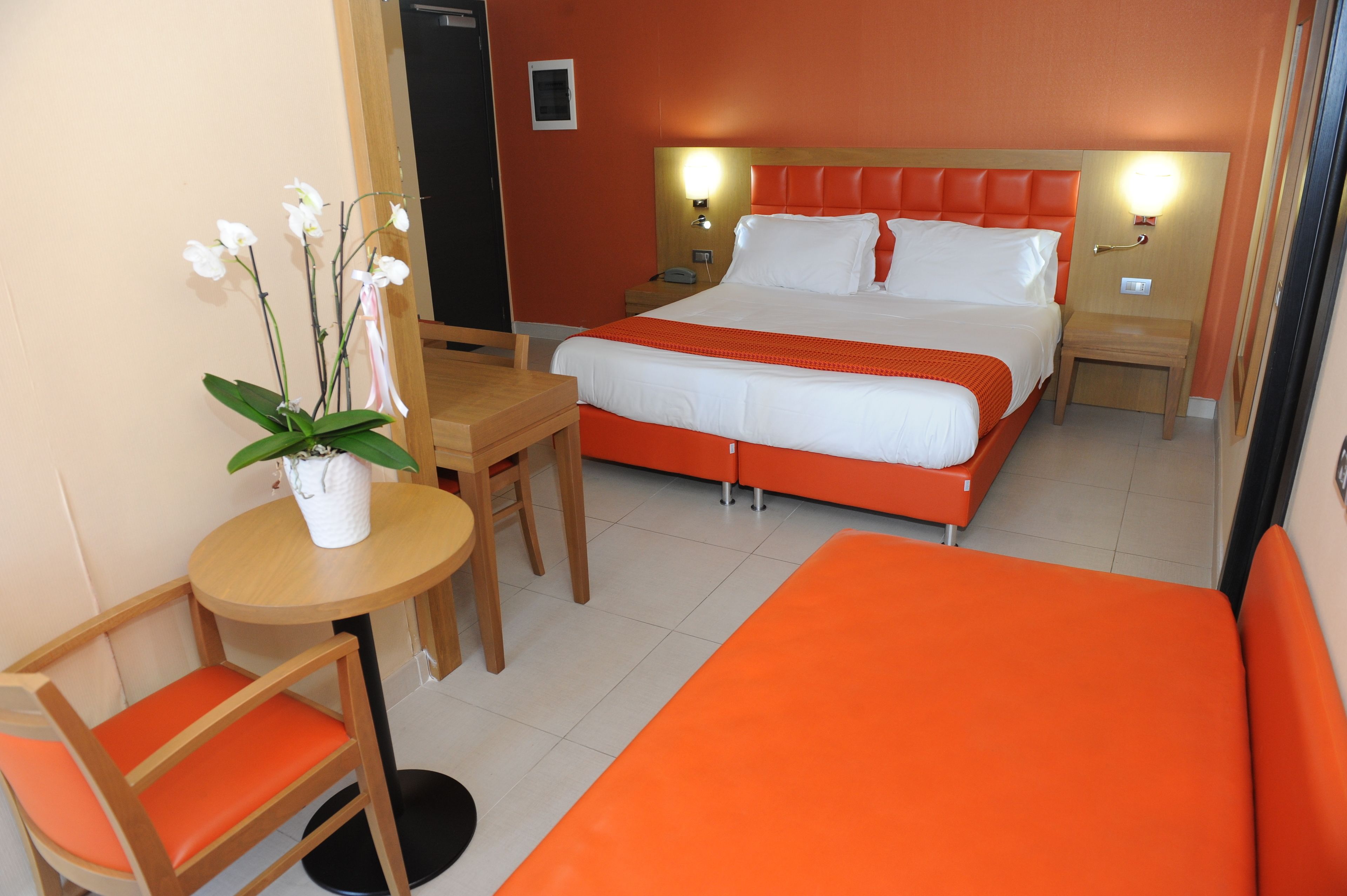 Habitación de hotel con cama, escritorio, silla y una mesita con planta en maceta.