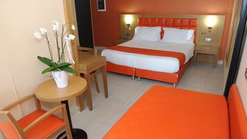 Habitación de hotel con cama, escritorio, silla y una mesita con planta en maceta.