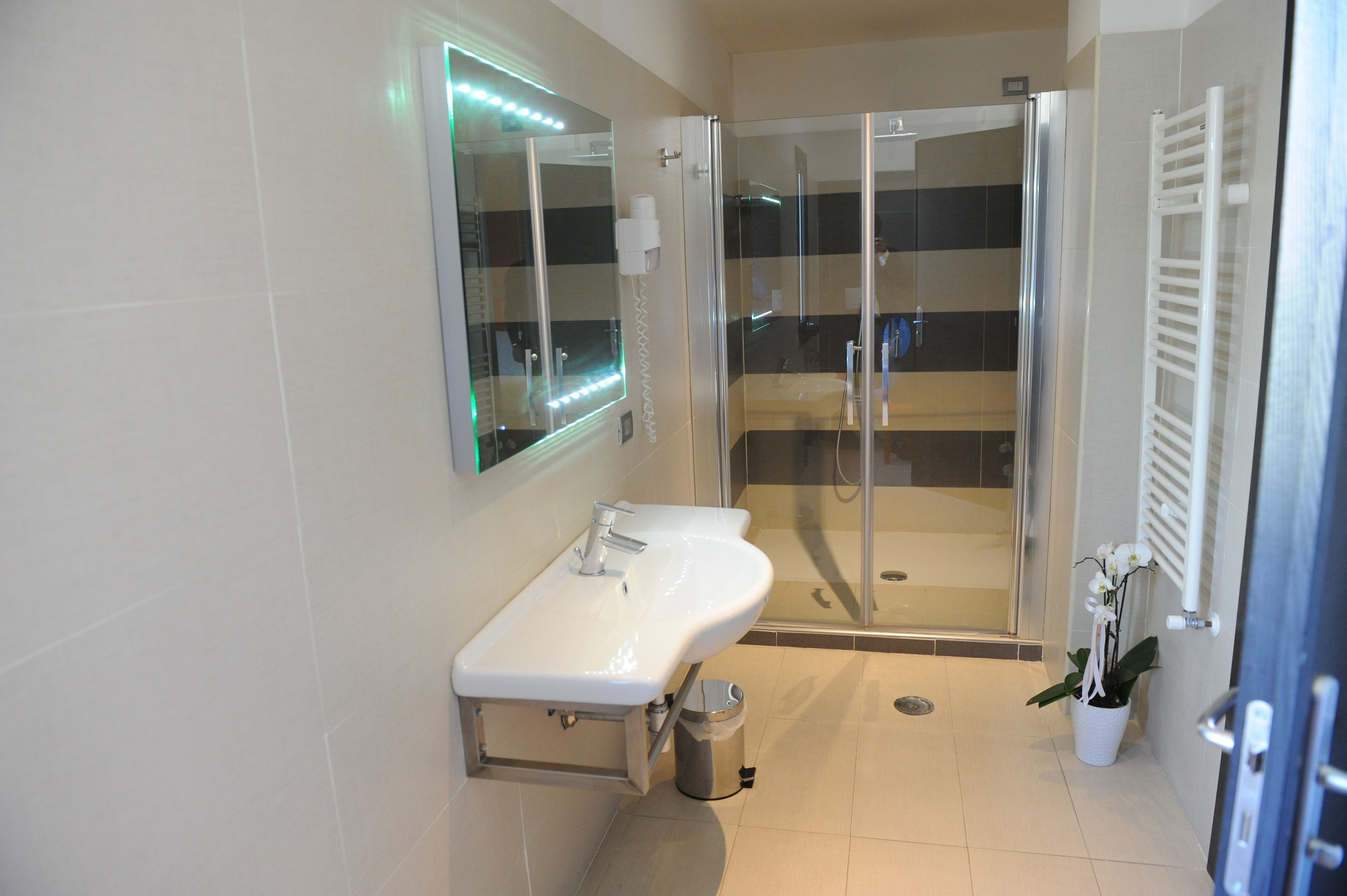Un baño moderno con ducha de vidrio, lavamanos blanco e iluminación LED en el espejo.