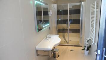 Un baño moderno con ducha de vidrio, lavamanos blanco e iluminación LED en el espejo.