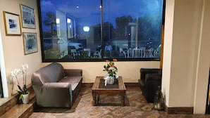 A living room with a large window, a sofa, a coffee table with flowers, and a potted plant. - Hotel Ristorante La Campagnola (Cassino)