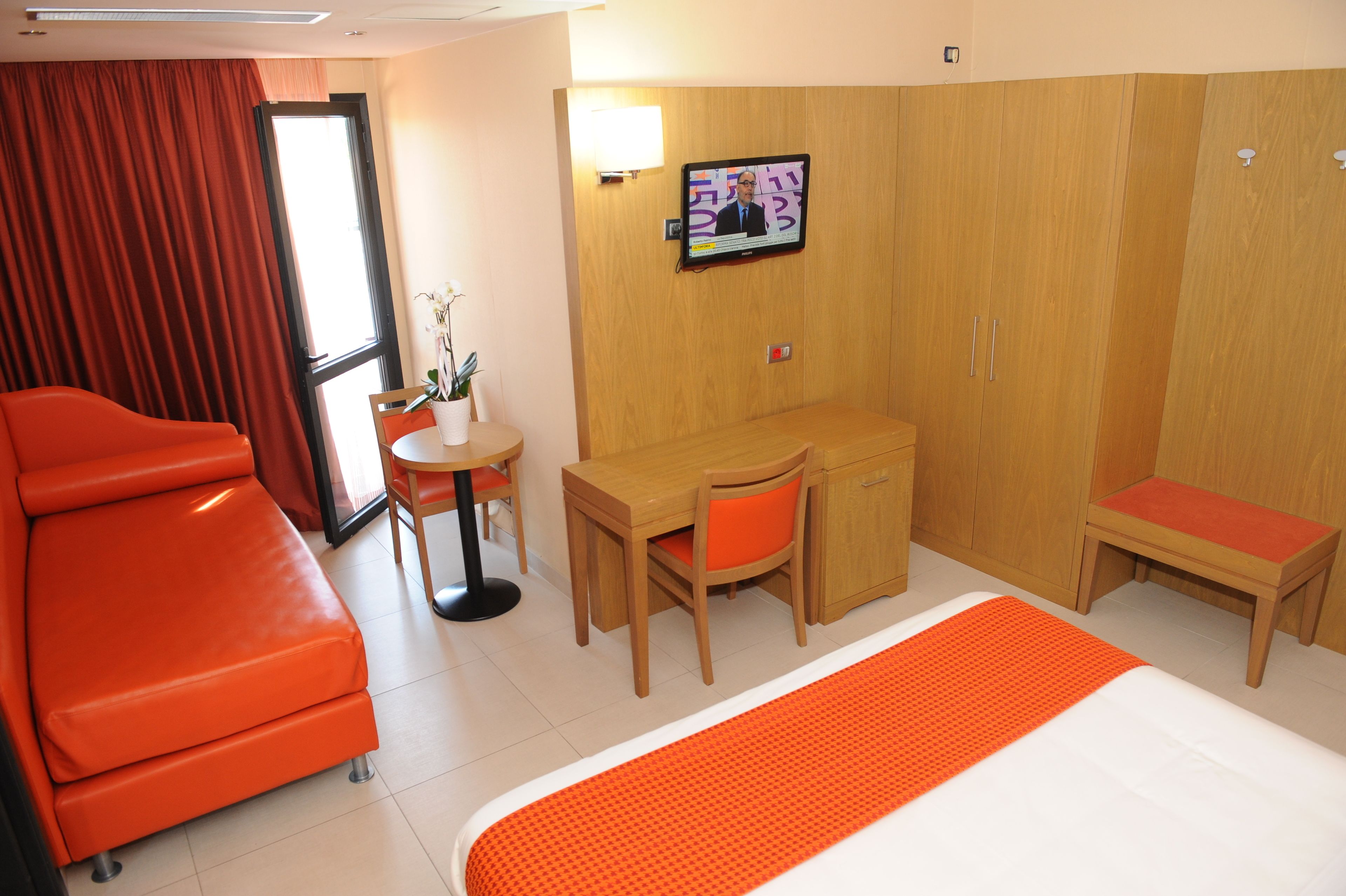 Quarto de hotel com cama, escrivaninha, cadeira, mesa pequena e guarda-roupa.