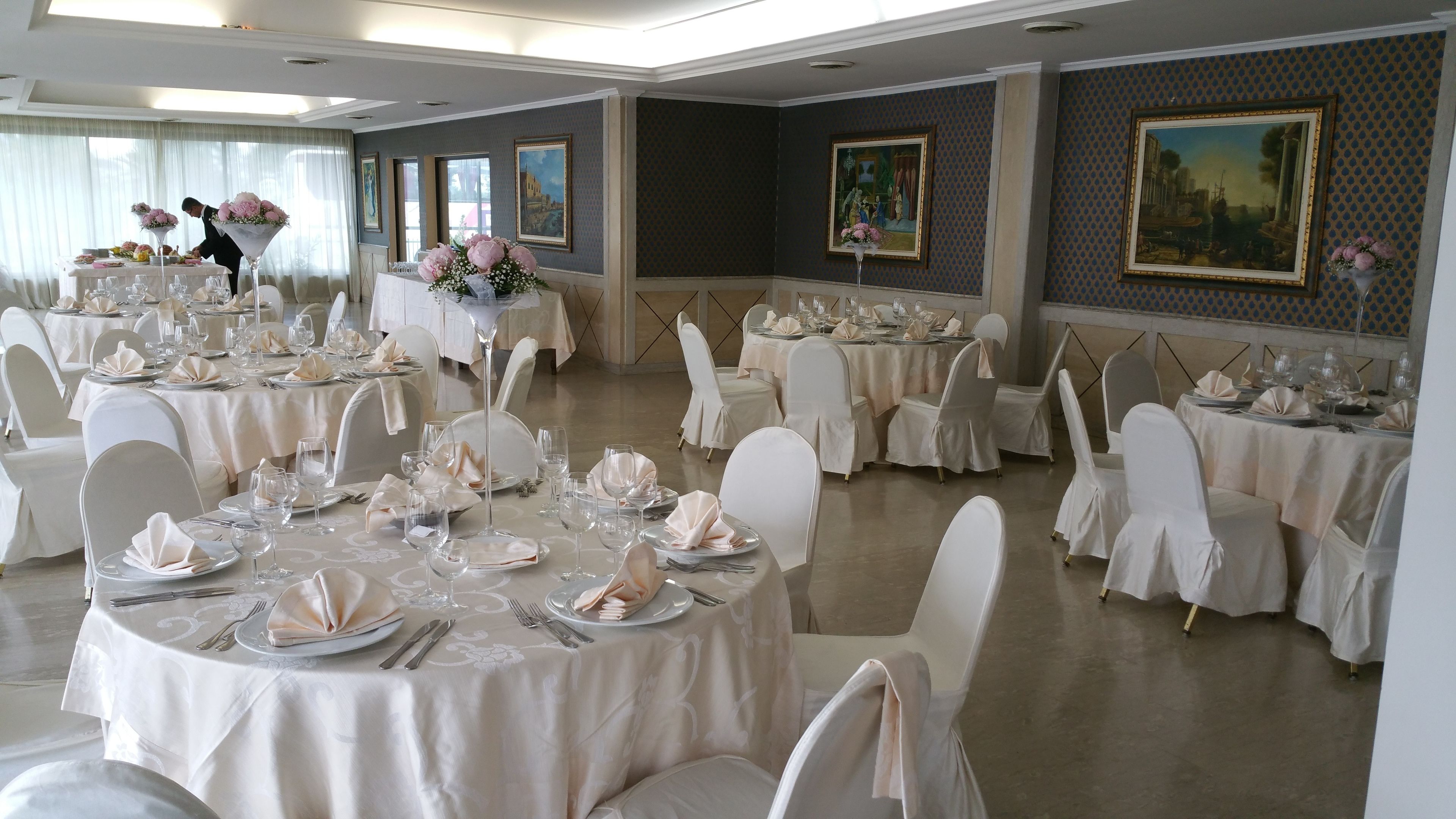 A banquet hall with round tables set for a formal event, featuring white tablecloths, chairs, and floral centerpieces.