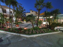 Un patio con mobiliario exterior, palmeras y un edificio con balcón.