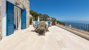 Um terraço com mesa e cadeiras, uma parede de pedra e vista para o mar.