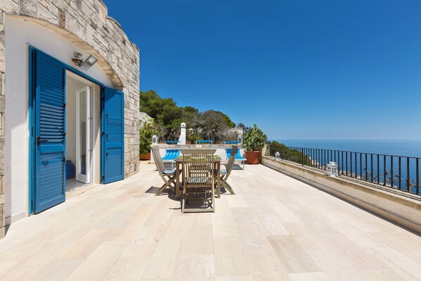 A terrace with a table and chairs, a stone wall, and a view of the sea.