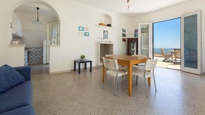 Uma sala de estar ampla com uma mesa de jantar, um sofá azul e vista para a varanda.