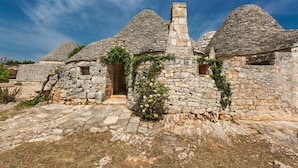 Un edificio de piedra con techos cónicos y un acceso central, rodeado por un camino de piedra.