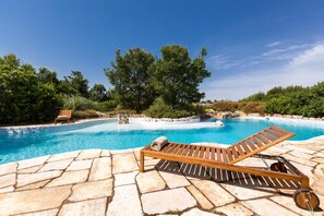 Un espace piscine avec un fauteuil de relaxation en bois et une terrasse en pierre.