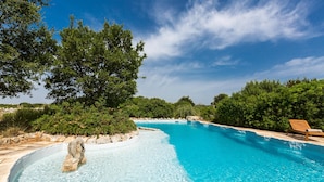 Una piscina azul cristalina rodeada de exuberante vegetación y una silla de lounge de madera.