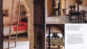 Una habitación rústica con una escalera de madera, cama con ropa de cama roja y pared de piedra.