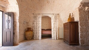Una habitación con pared de piedra, una cama, un aparador de madera y un jarrón grande.