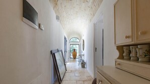 Un pasillo estrecho con suelo de baldosas, un jarrón grande al final y un mueble con objetos decorativos.