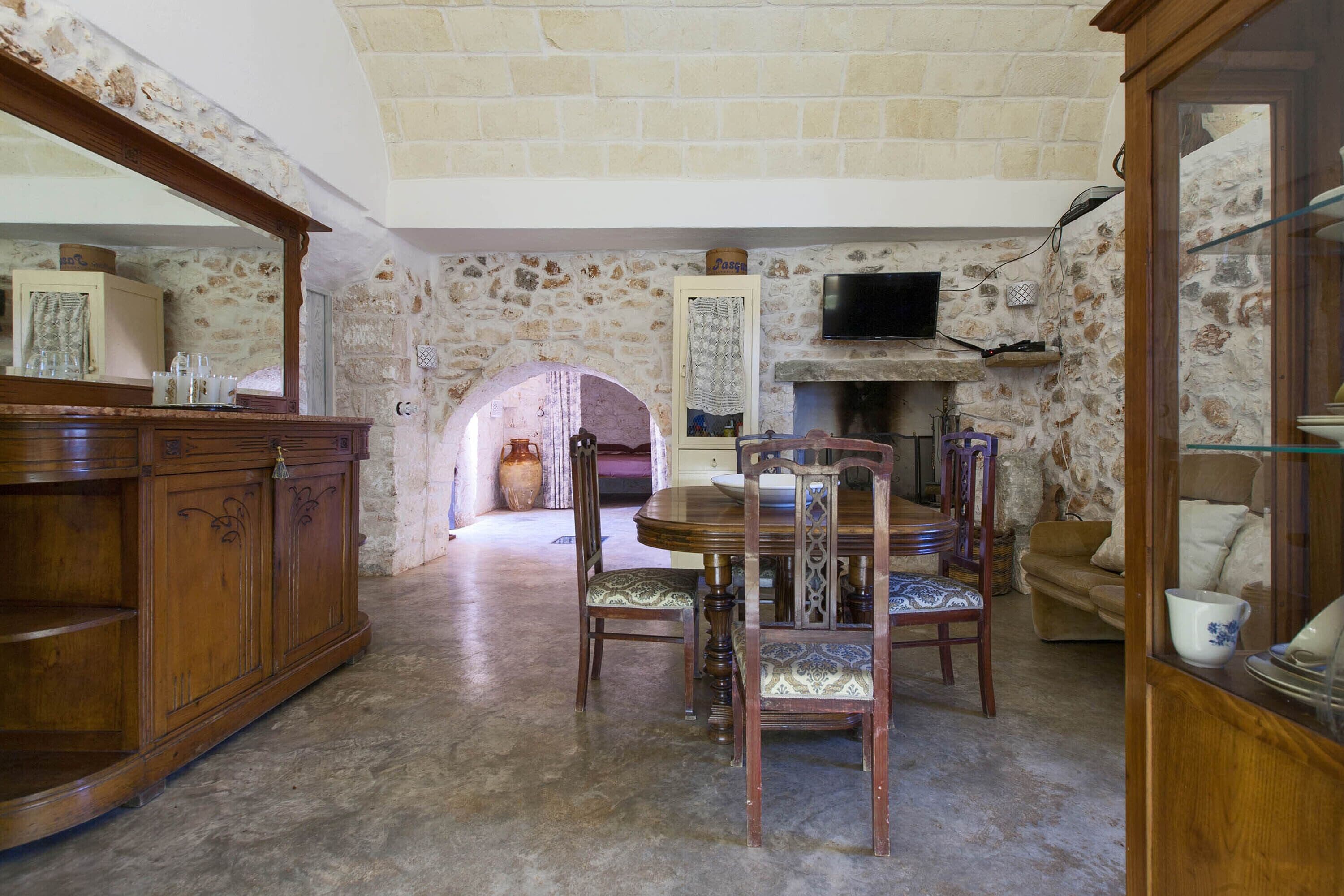 A dining area with a stone wall, wooden furniture, and a television mounted above a fireplace.