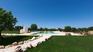 Una piscina rodeada de césped, rocas grandes y algunos árboles.