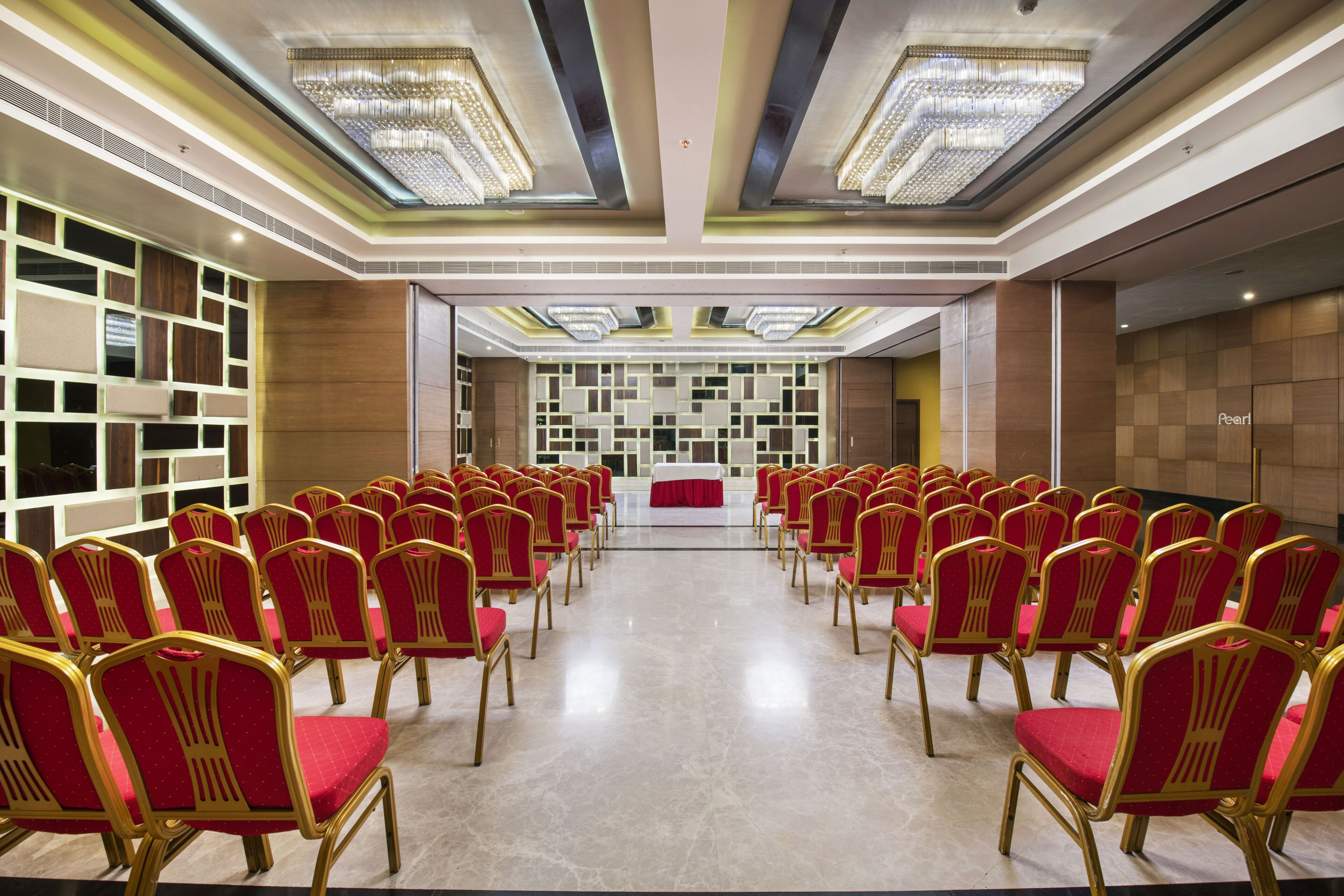 A conference room with rows of red and gold chairs facing a stage with a white table and a red cloth.