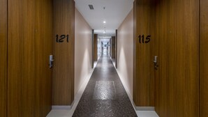 A hallway with wooden doors numbered 121 and 115, leading to a bright, well-lit corridor. - Hotel Satkar Grande (Thane)