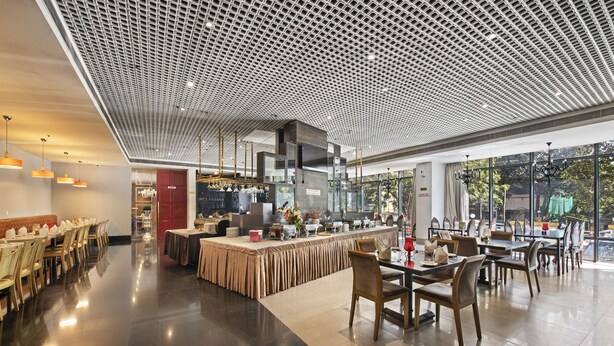 A modern restaurant with a high ceiling, polished floors, and a central bar area. - Hotel Satkar Grande (Thane)