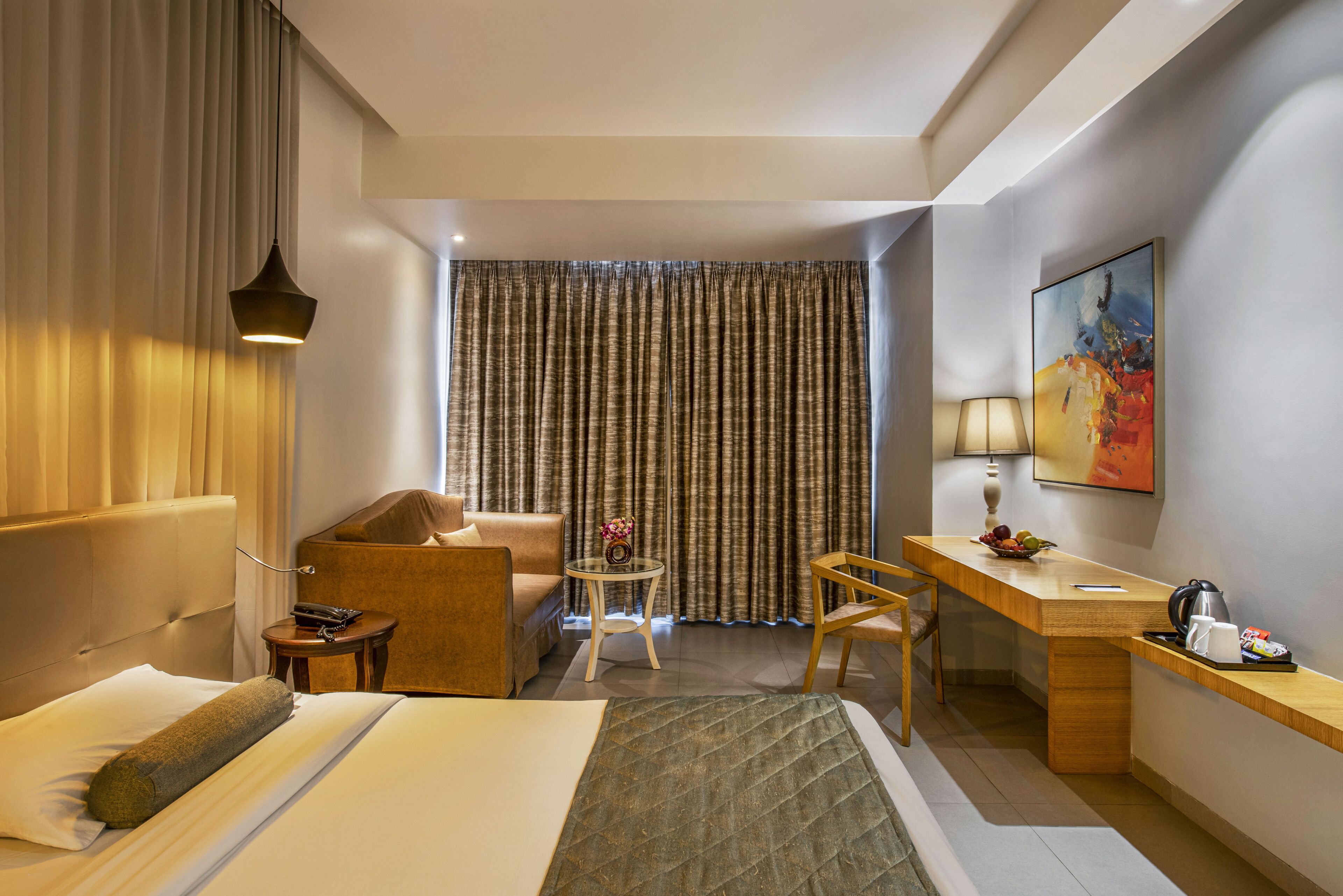 Una habitación de hotel con cama, escritorio, silla, una mesita y un cuadro en la pared.