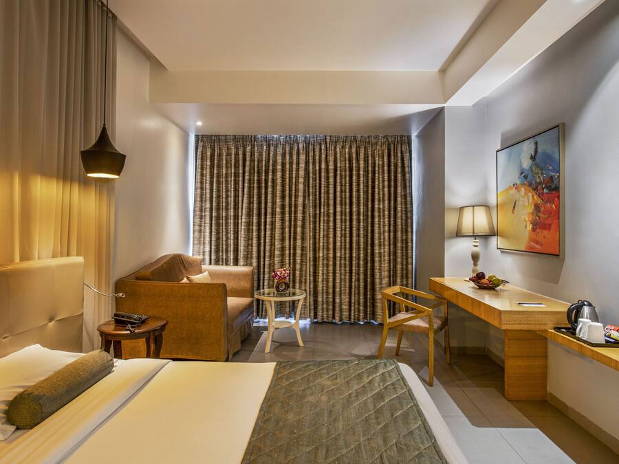 Una habitación de hotel con cama, escritorio, silla, una mesita y un cuadro en la pared.