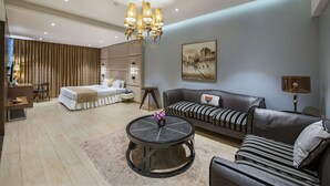 A modern hotel room with a bed, a sofa, a round coffee table, and a chandelier. - Hotel Satkar Grande (Thane)