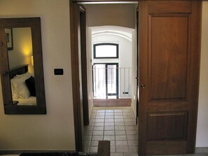 Un couloir avec une porte en bois, un sol carrelé et un lit recouvert de draps blancs.