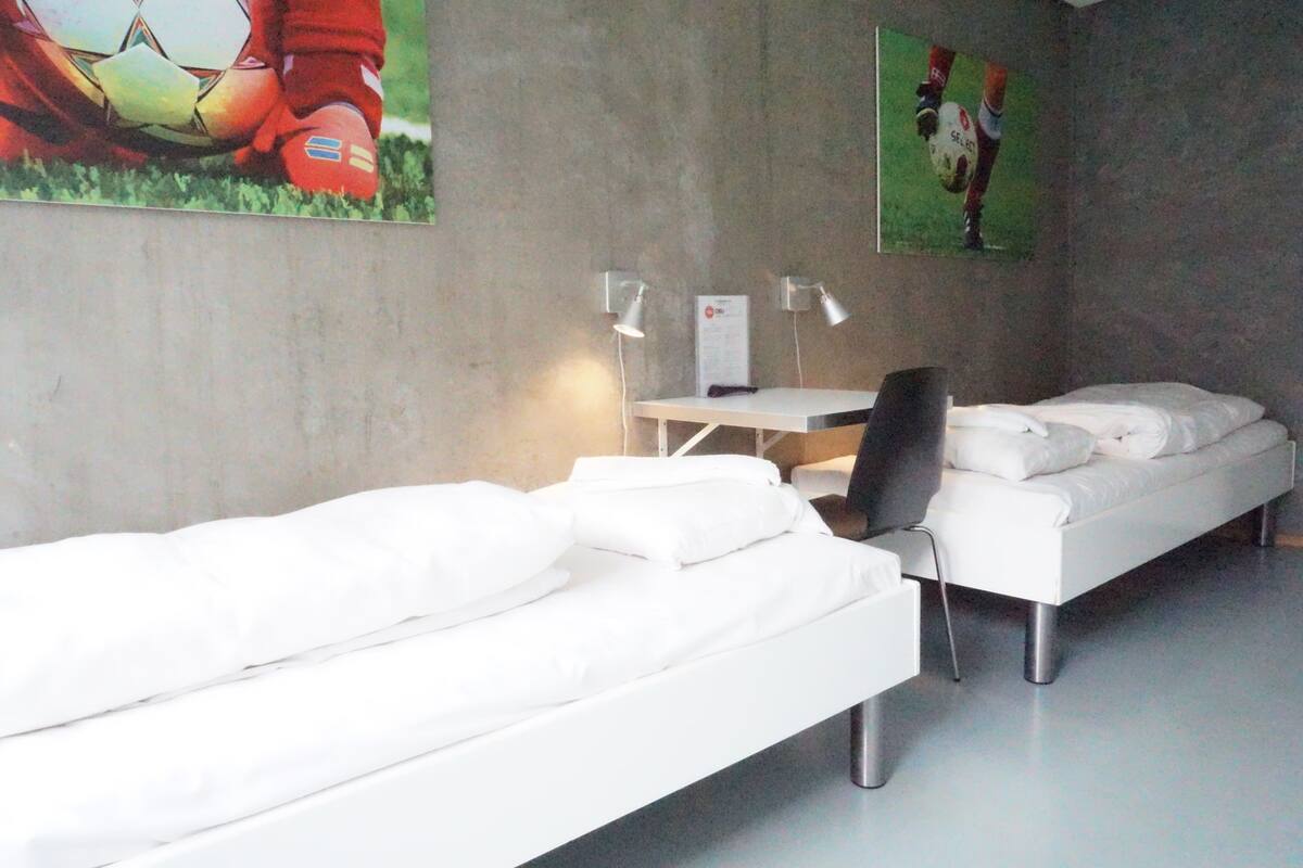 Una habitación de hotel moderna con una cama blanca, un escritorio con dos lámparas y una silla. Hay carteles en la pared.