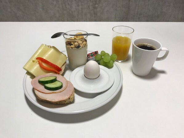 Un plato de desayuno con jamón, queso, pepino, huevo y un vaso de jugo de naranja.