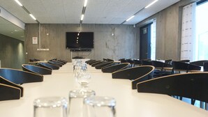 Una sala conferenze con un lungo tavolo, sedie e un televisore appeso al muro.