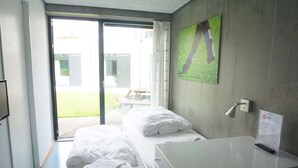 Camera d'albergo con un letto, una scrivania, una finestra con tende, una TV a parete e un cartello sulla scrivania.