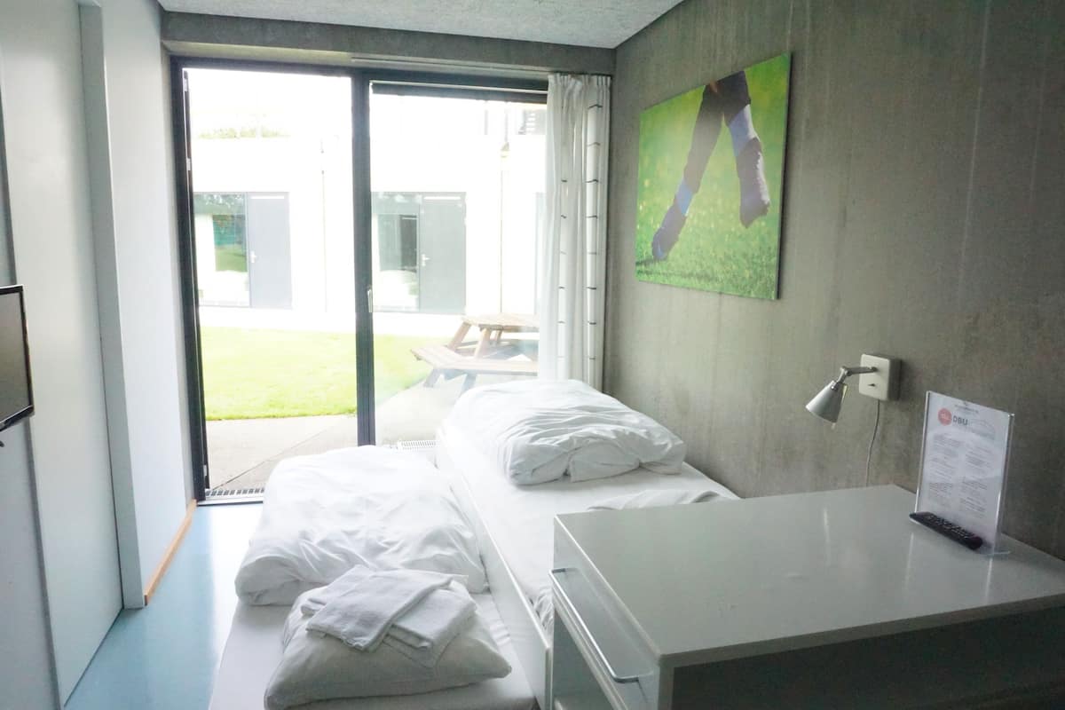 Habitación de hotel con cama, escritorio, ventana con cortinas, televisor montado en la pared y un cartel en el escritorio.