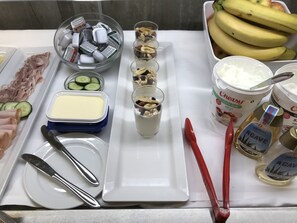 Una mesa con alimentos, incluyendo pepinos en rodajas, un recipiente de mantequilla, un vaso de leche, un envase de yogur, un tarro de miel y una botella de jarabe.