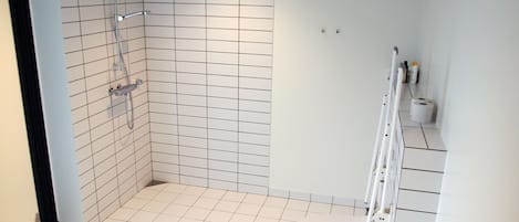 A bathroom with white tiled walls and floor, a shower, a toilet, and a white ladder.