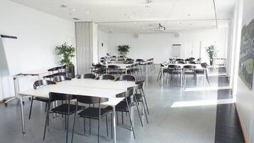 Un salón de conferencias con una gran mesa y sillas, paredes blancas y proyectores instalados en el techo.