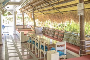 Un ristorante con tetto di paglia, mobili in legno e pavimento a scacchi.