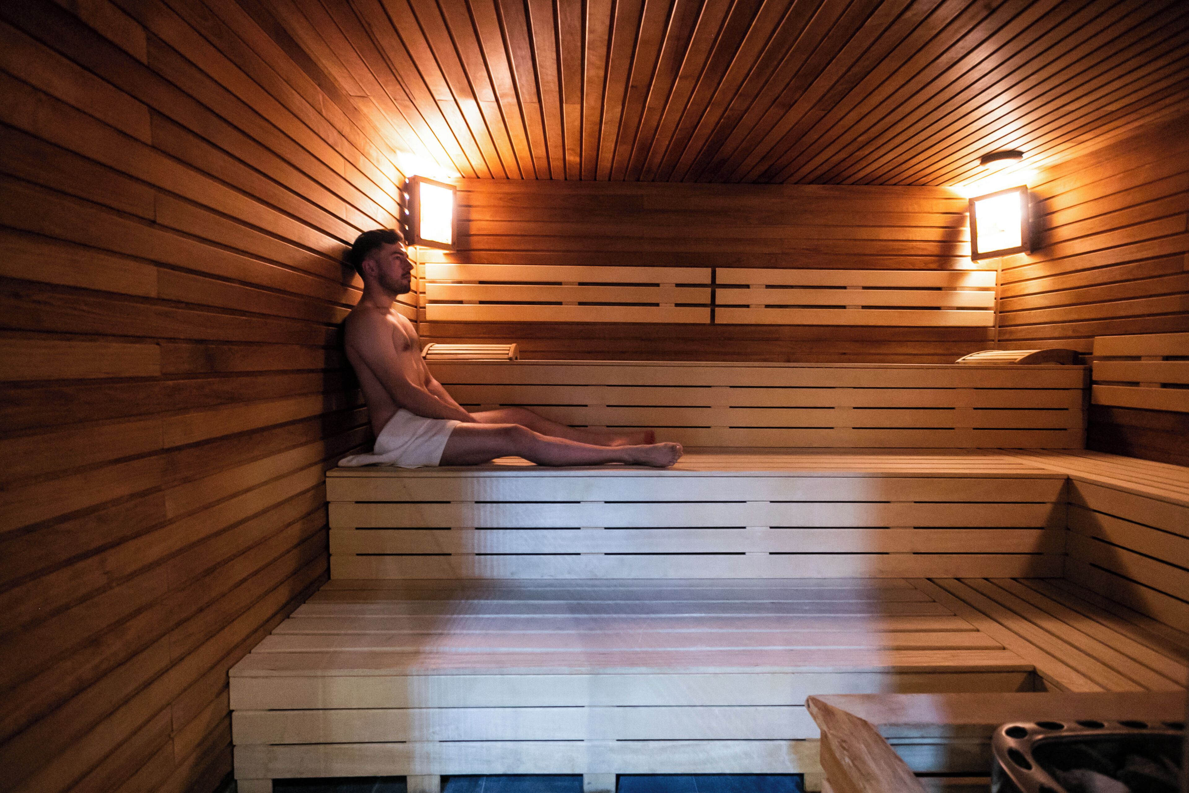 Eine Sauna mit Holzbänken und -wänden, zwei Wandleuchten und einer Bank mit Handtuch.