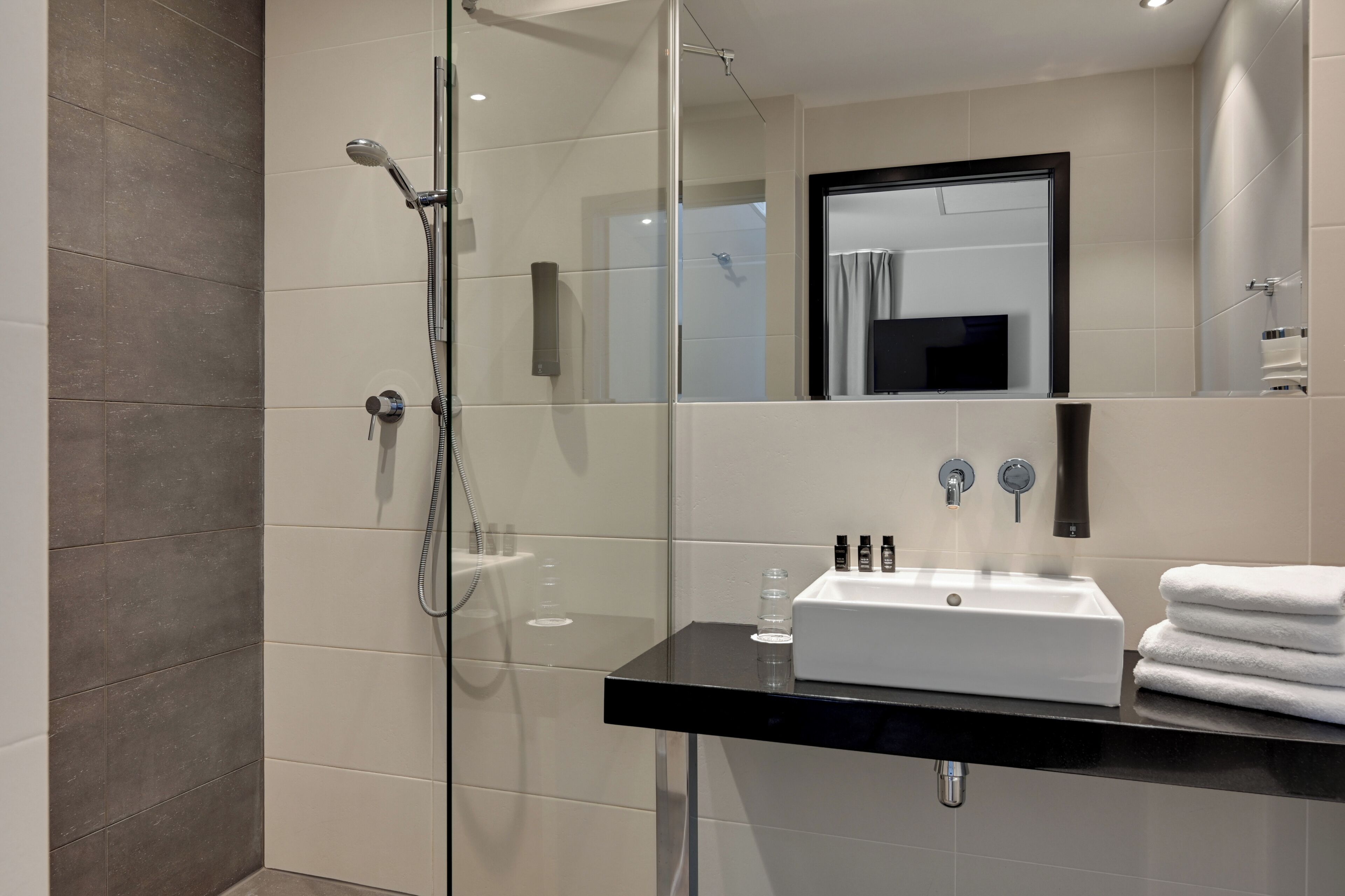 A modern bathroom with a glass-enclosed shower, a black countertop sink, and a mirror above it.