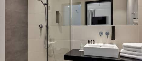 Un baño moderno con ducha envuelta en vidrio, un lavabo con encimera negra y un espejo sobre él.