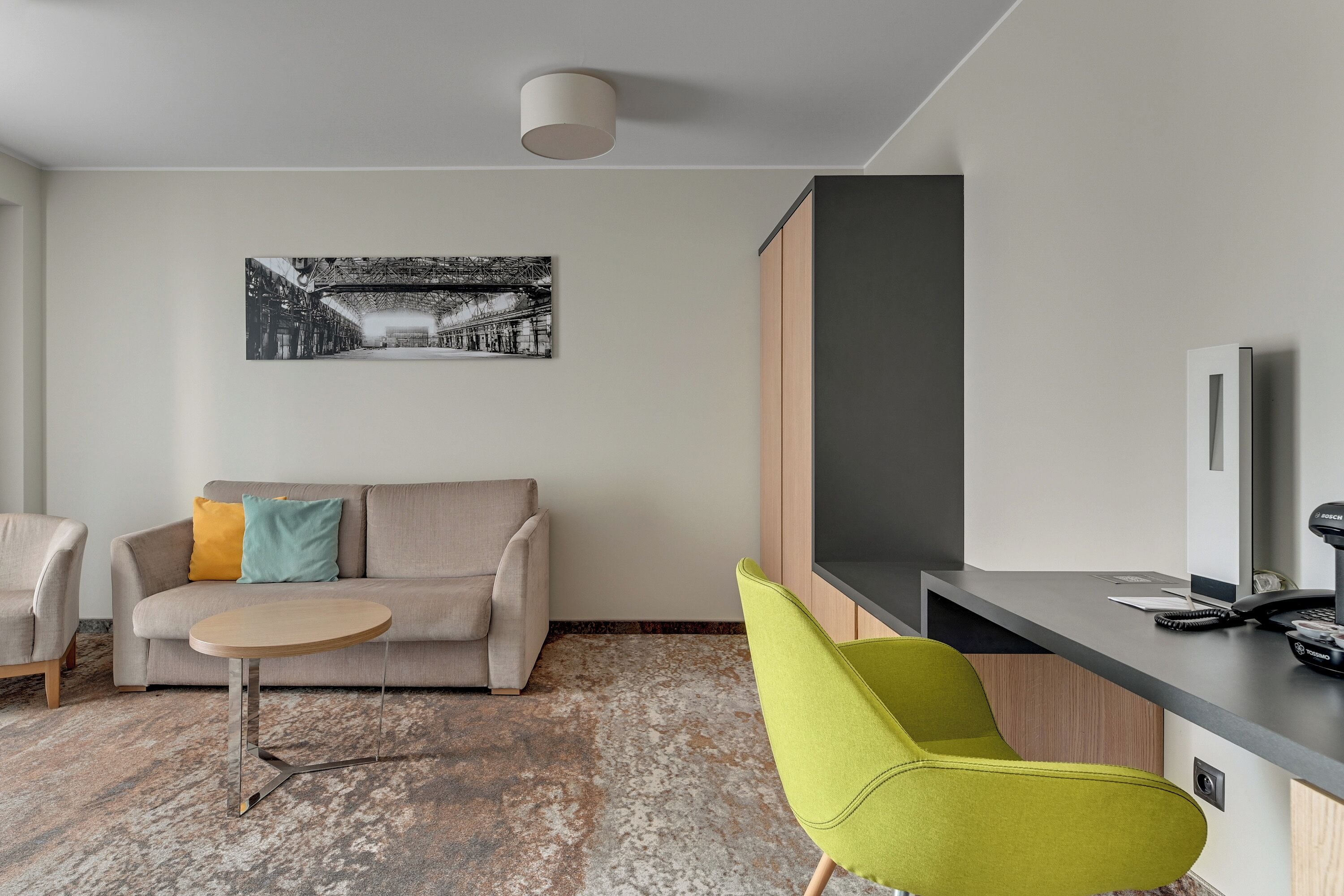 Una sala de estar moderna con un sofá, una mesa redonda, un sillón verde brillante, un televisor de pantalla plana y un cuadro en la pared.